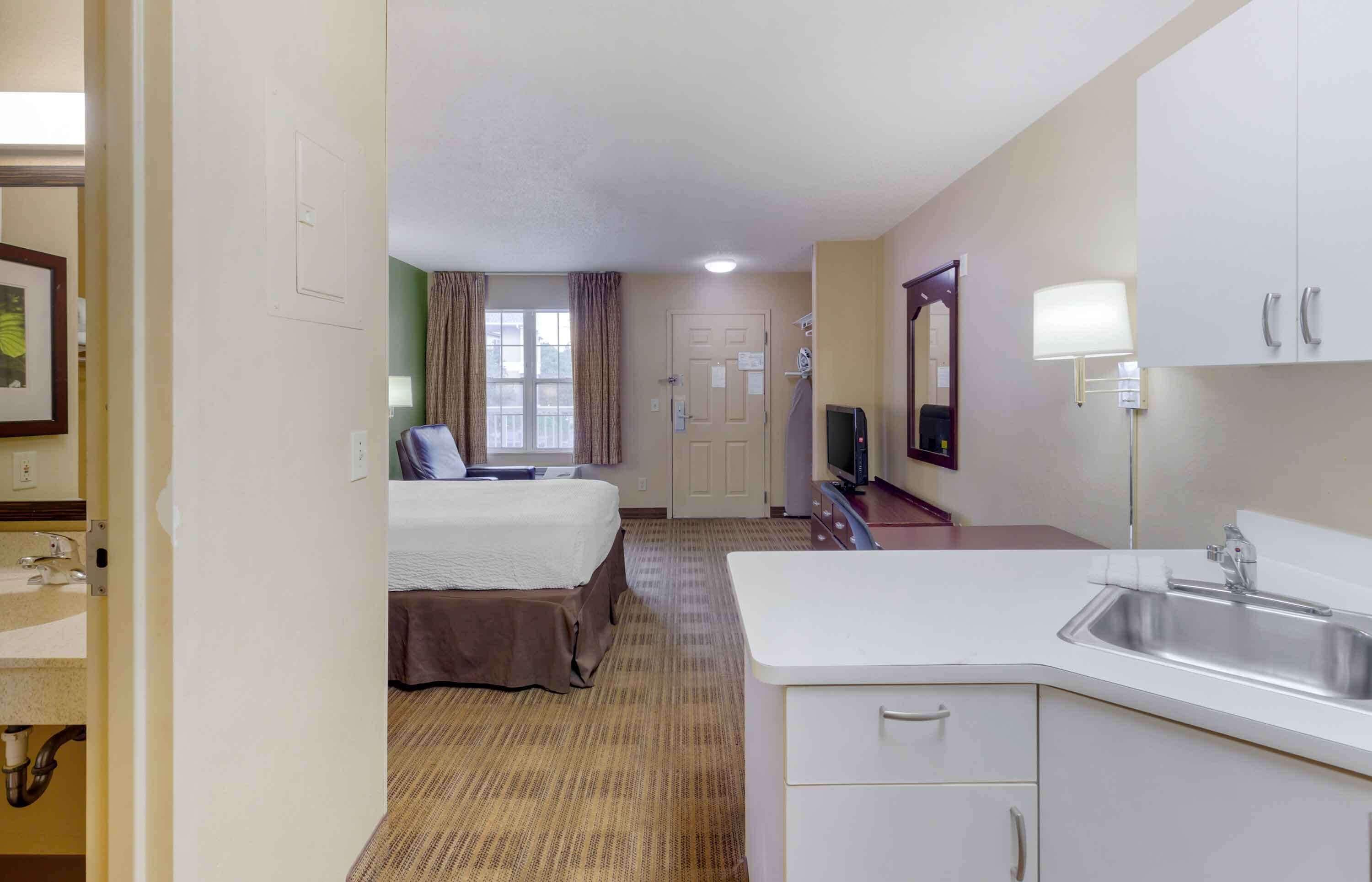 Una habitación de hotel con una cama, un escritorio, un televisor, un lavamanos y un espejo.