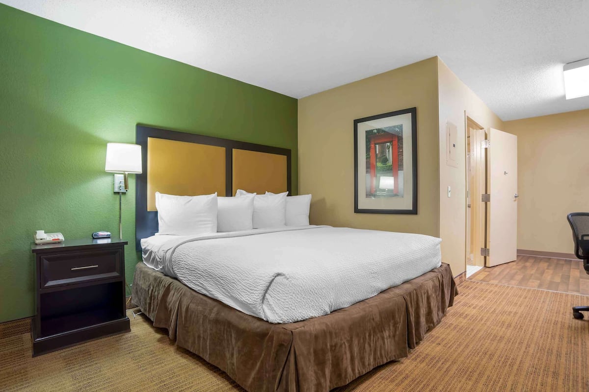 Una camera d'albergo con un letto grande, un comodino con una lampada, un quadro appeso alla parete e una porta che conduce a un'altra stanza.