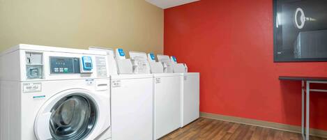A laundry room with a washing machine and dryers, wooden flooring, and a red wall.