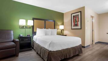 A hotel room with a large bed, green walls, a brown leather chair, and two bedside lamps.