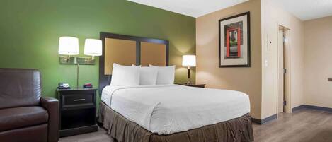 A hotel room with a large bed, green walls, a brown leather chair, and two bedside lamps.
