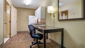 Une chambre d’hôtel équipée d’un bureau, d’une chaise, d’une kitchenette et d’un miroir.
