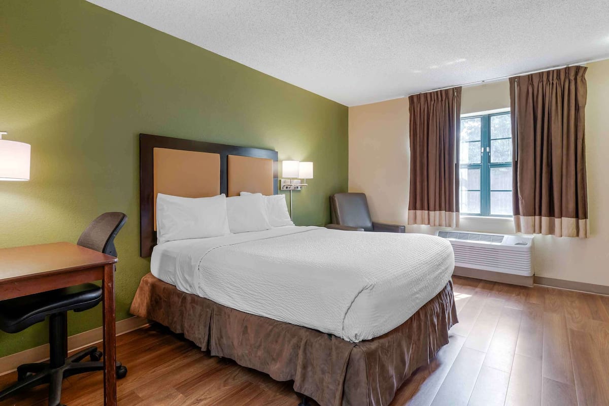 Habitación de hotel con cama, escritorio, silla y ventana con cortinas.