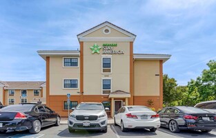 A Stay America hotel with a beige facade, multiple windows, and a parking lot with several cars.