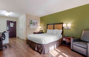 A hotel room with a bed, desk, chair, and a painting on the wall.