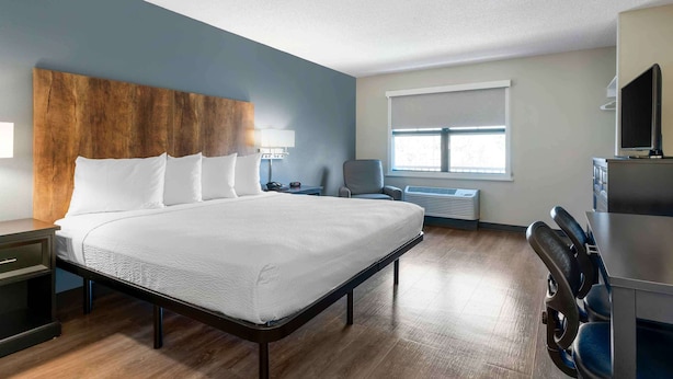 Habitación de hotel con una cama grande, cabecera de madera, escritorio con silla, televisor y ventana con persianas.