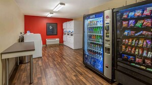 Ein Hotelzimmer mit Holzboden, einem weißen Schreibtisch, einem Kühlschrank, einer Verkaufsmaschine und einer roten Akzentwand.