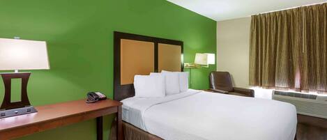 A hotel room with a large bed, a desk with a telephone, a chair, and a window with curtains.