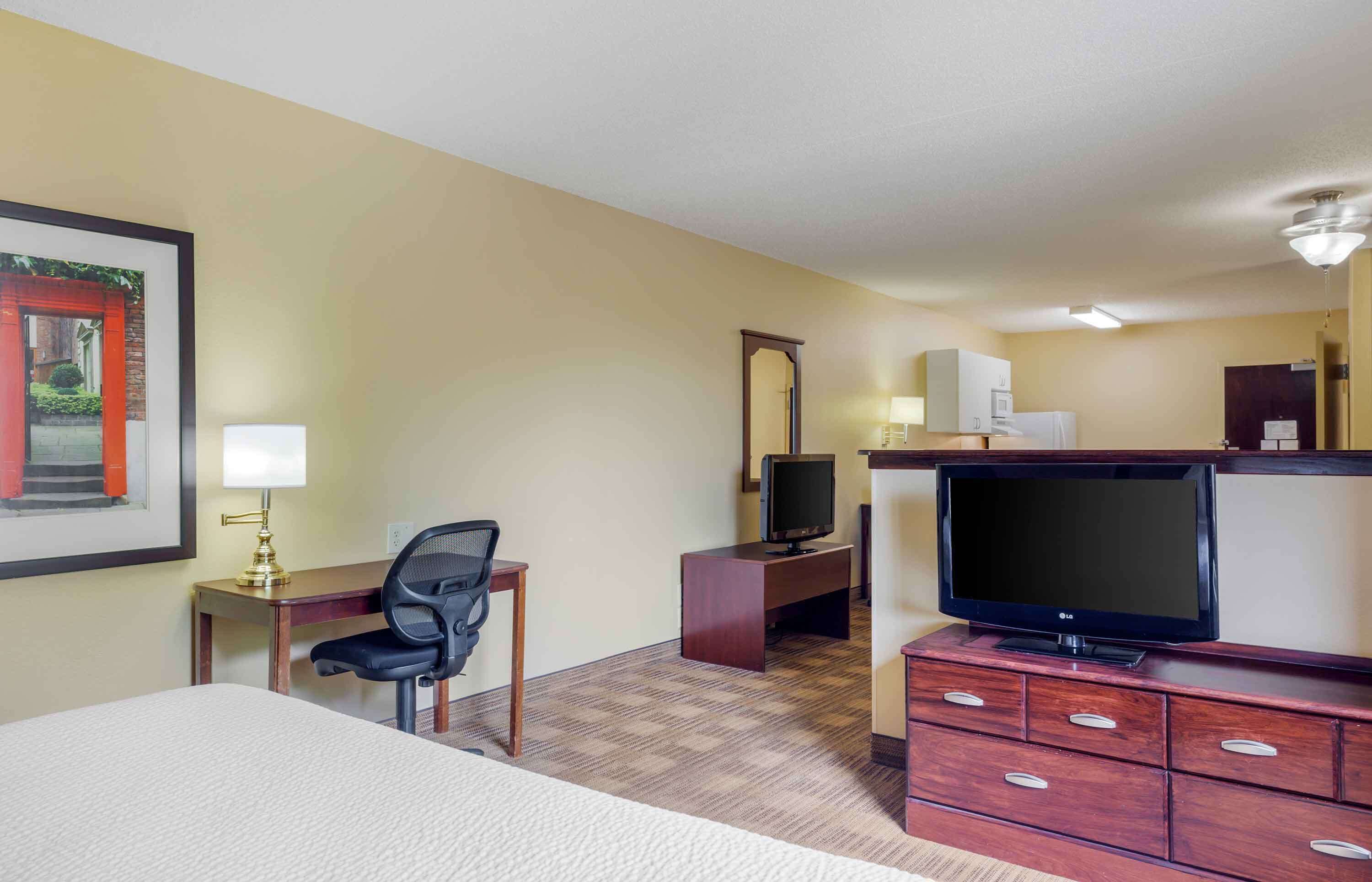 A hotel room with a bed, desk, chair, TV, and a mirror.