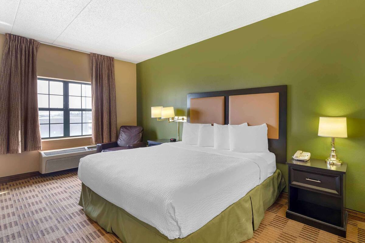 A hotel room with a large bed, two bedside lamps, a nightstand with a phone, and a window with curtains.