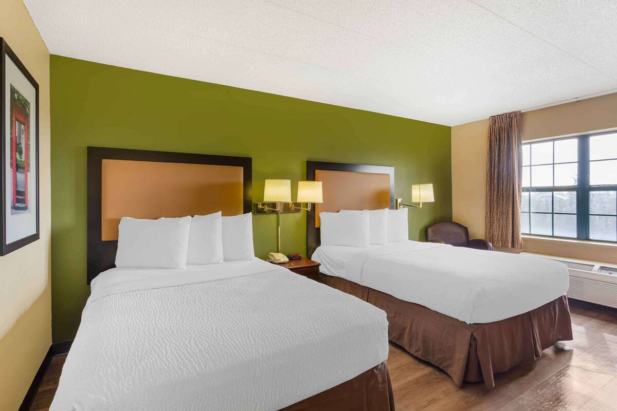 A hotel room with two beds, green walls, and a large window.