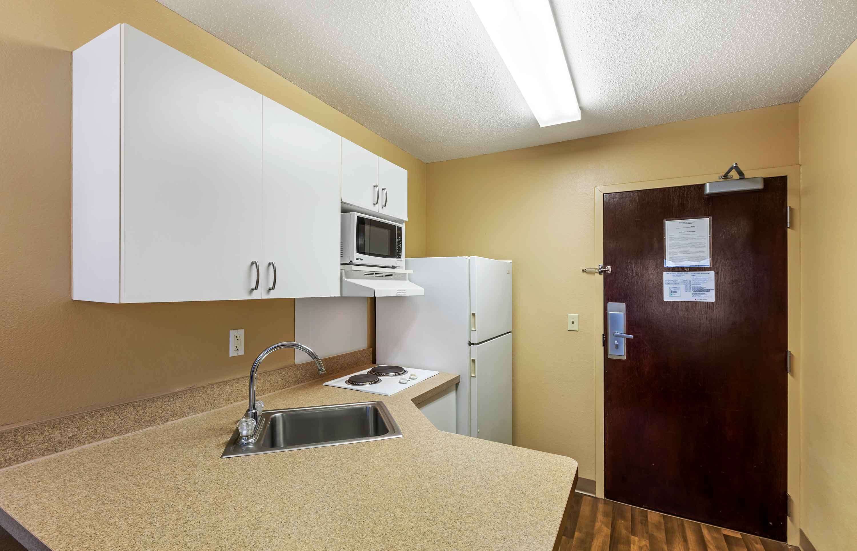 A compact kitchen with white cabinets, a microwave, a refrigerator, and a sink.