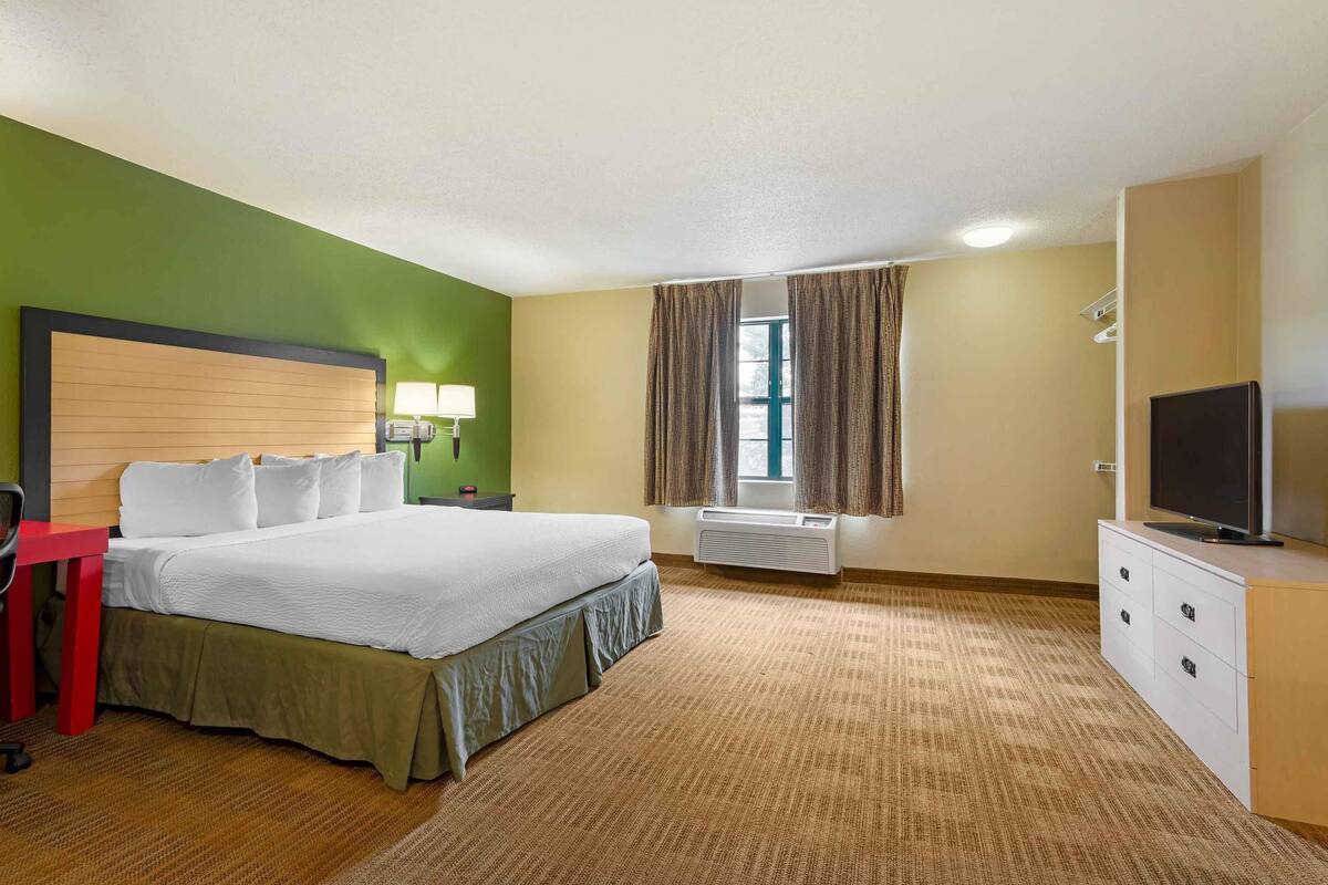 A hotel room with a bed, a desk, a chair, a TV, and a window with curtains.