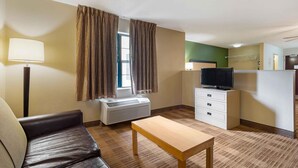 A hotel room with a leather sofa, a wooden table, a TV on a stand, a heater, a wardrobe, and a window with curtains. - Extended Stay America Select Suites - Atlanta - Duluth (Duluth)