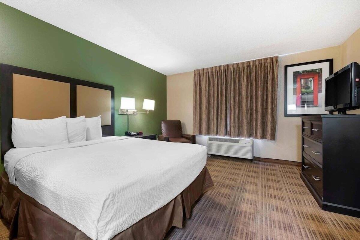 A hotel room with a large bed, a desk with a chair, a television, a dresser, and a framed picture on the wall.