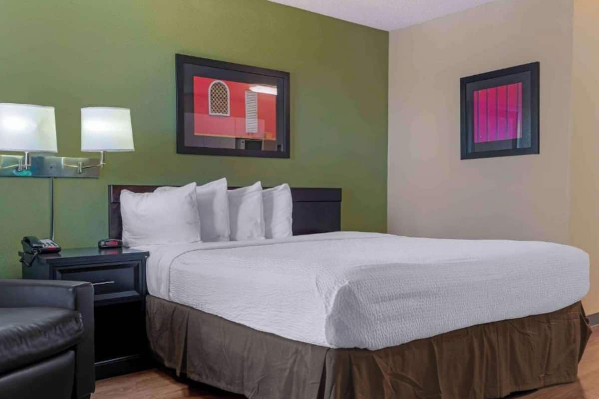 A hotel room with a bed, a nightstand, a lamp, and a chair.