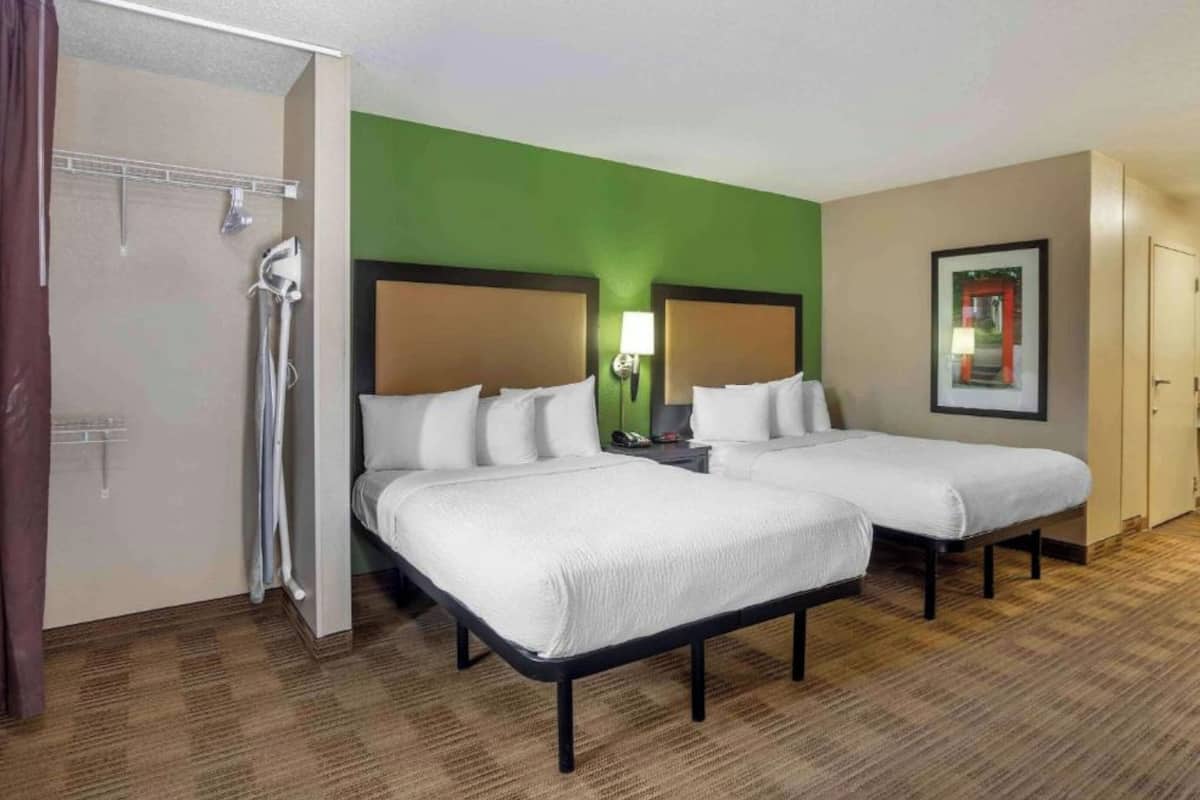 A hotel room with two beds, a shower, a green accent wall, a framed picture, and a door.