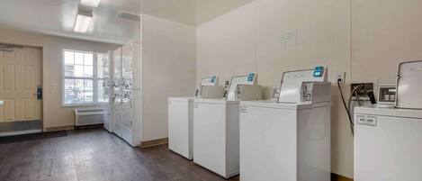 A laundry room with four white washing machines, a large window, and a door.