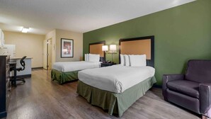 Habitación de hotel con dos camas, un escritorio, una silla y una pared de acento verde.