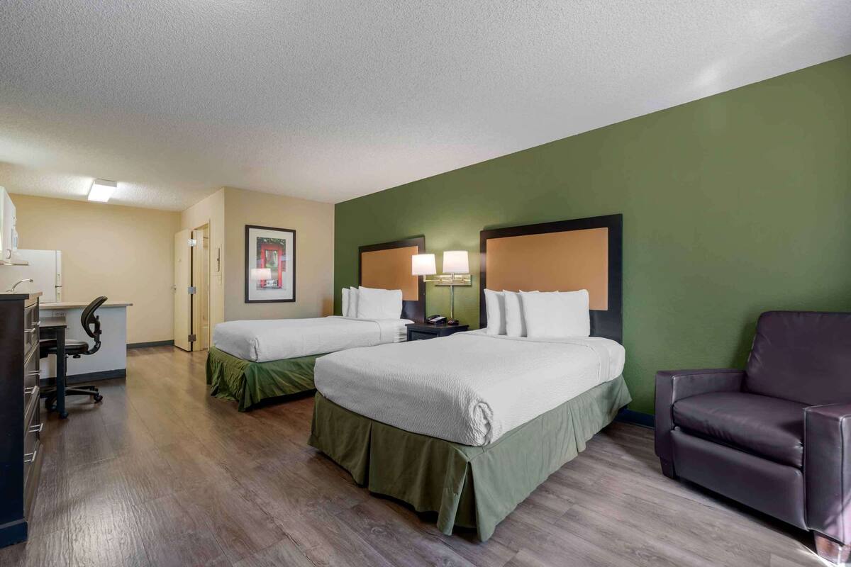 A hotel room with two beds, a desk, a chair, and a green accent wall.