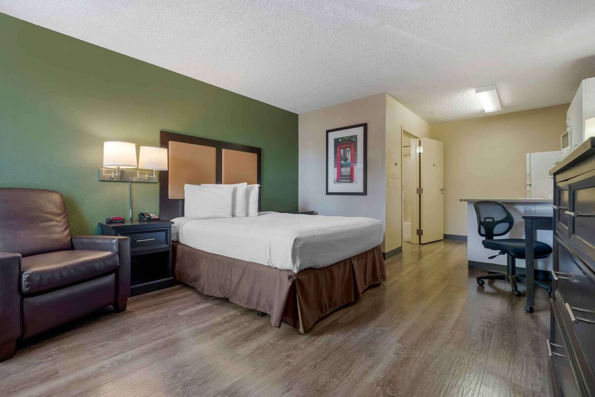 A hotel room with a bed, a desk, a chair, a nightstand, and a lamp.