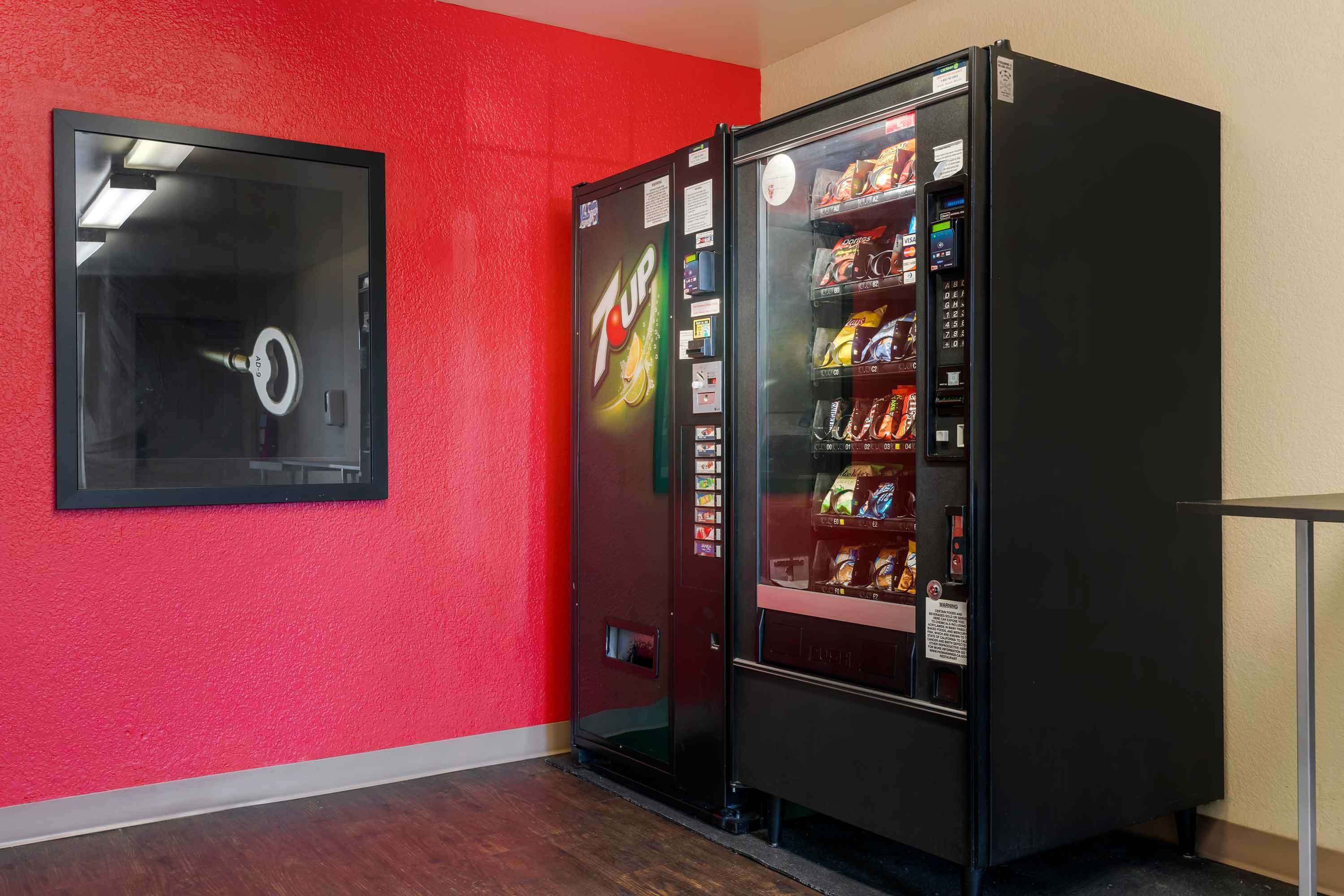 Ein Zimmer mit roter Wand, einem schwarzen Automaten und einem gerahmten Bild.