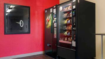 A room with a red wall, a black vending machine, and a framed picture on the wall.