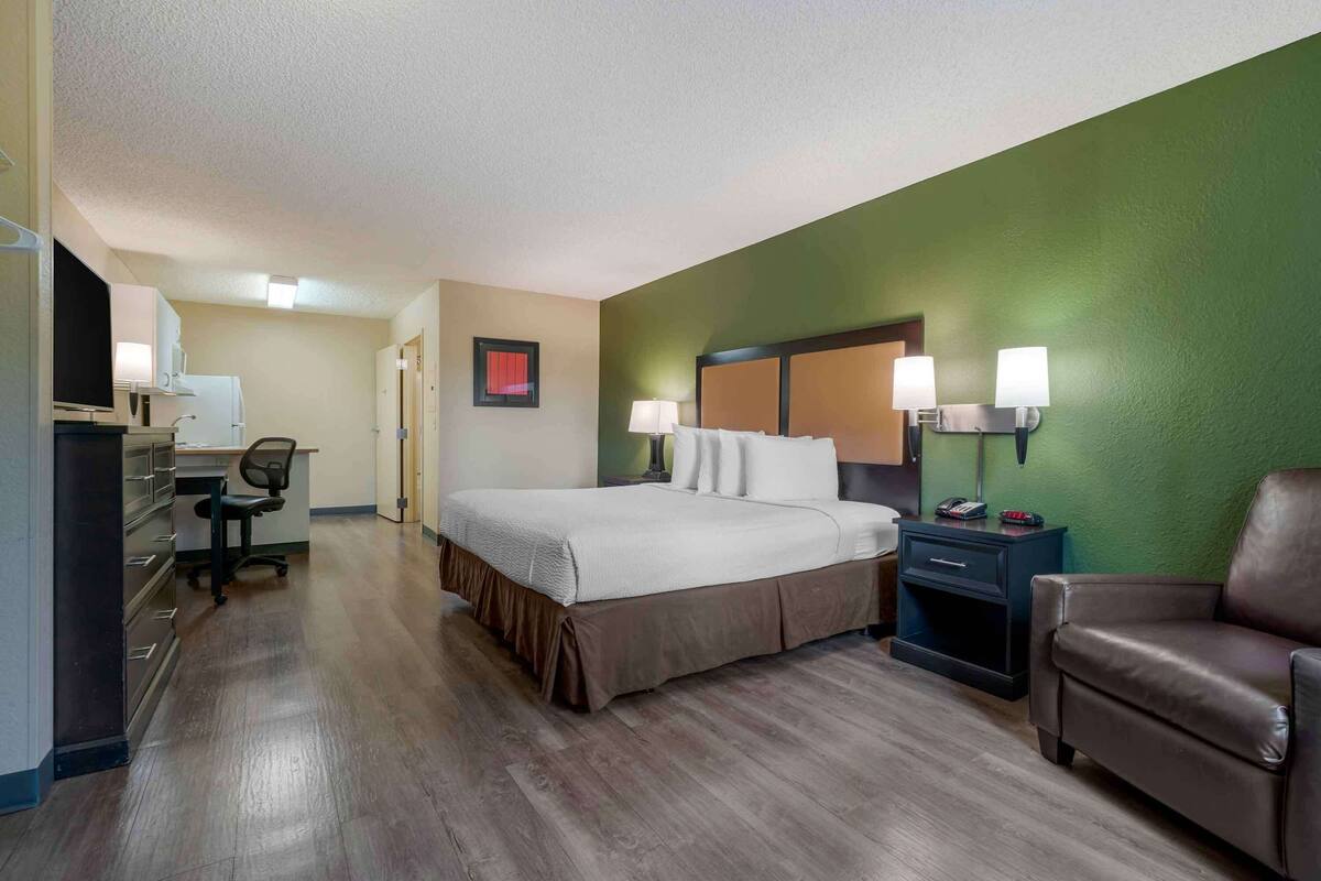 A hotel room with a bed, desk, chair, and a green accent wall.
