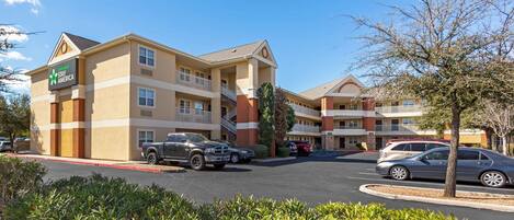 A Stay America hotel with a two-story structure, multiple balconies, and a parking lot with several cars.