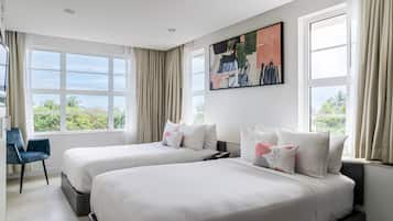 Habitación de hotel con dos camas, un escritorio y una silla. Cuenta con un ventanal con cortinas y un cuadro en la pared.