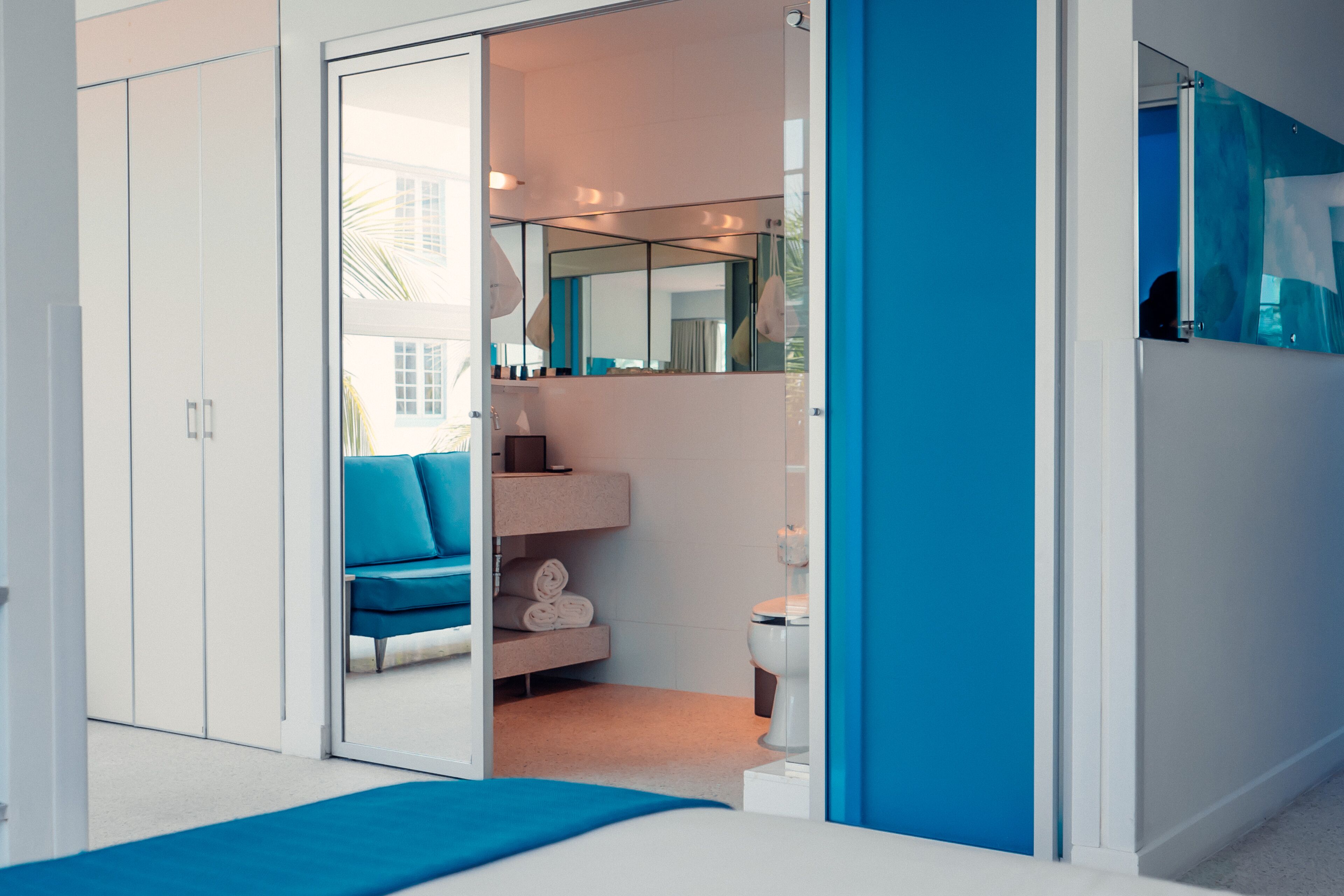 A modern bathroom with a glass door, a blue bench, a white toilet, and a mirror.