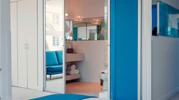 A modern bathroom with a glass door, a blue bench, a white toilet, and a mirror.