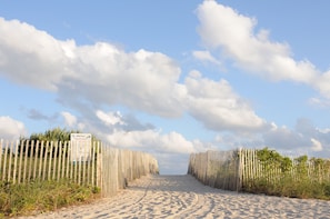 A sandy beach path flanked by wooden fences with a signboard.