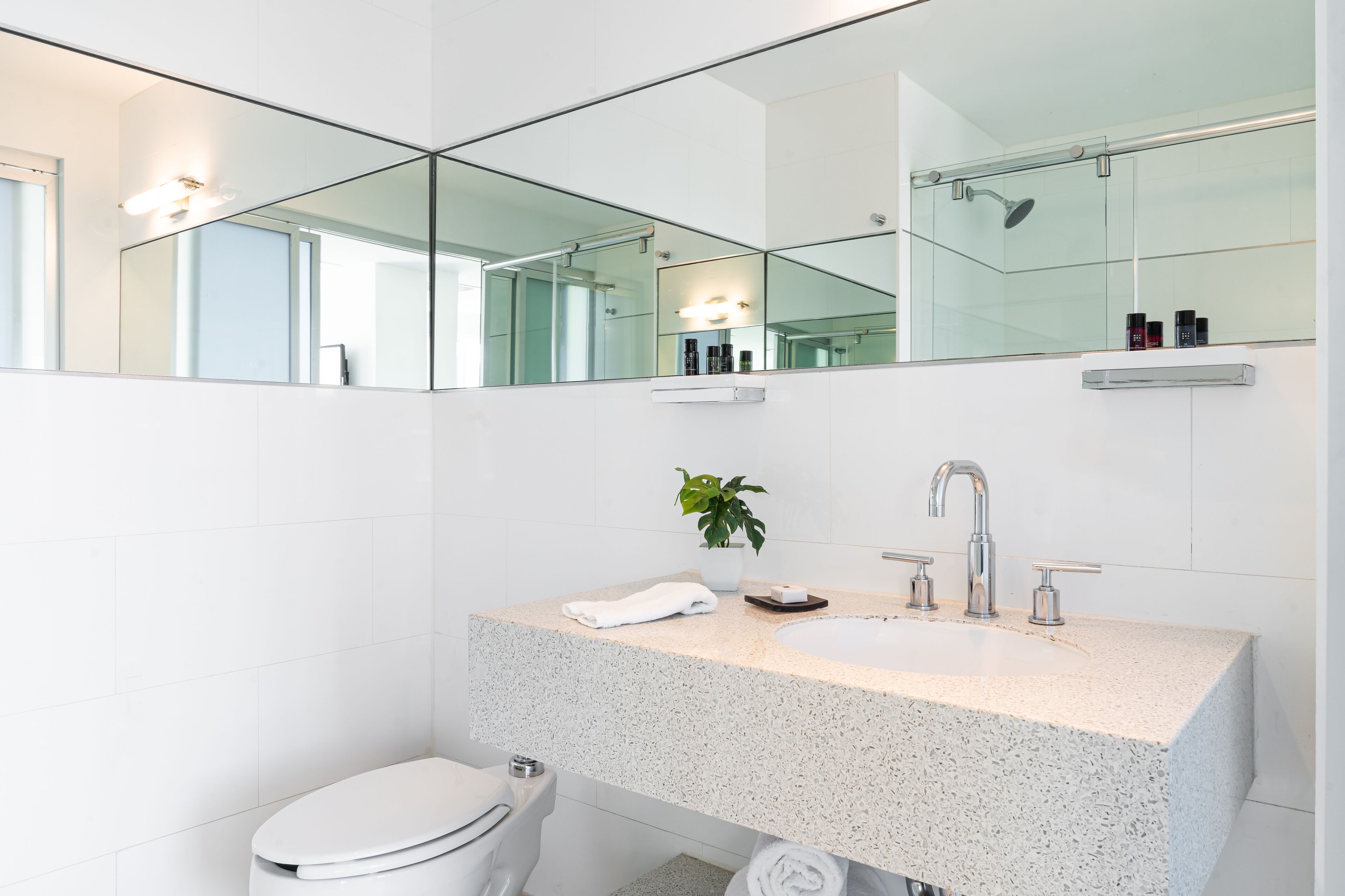 A modern bathroom with a freestanding toilet, a sink with a granite countertop, and a large mirror above the sink.
