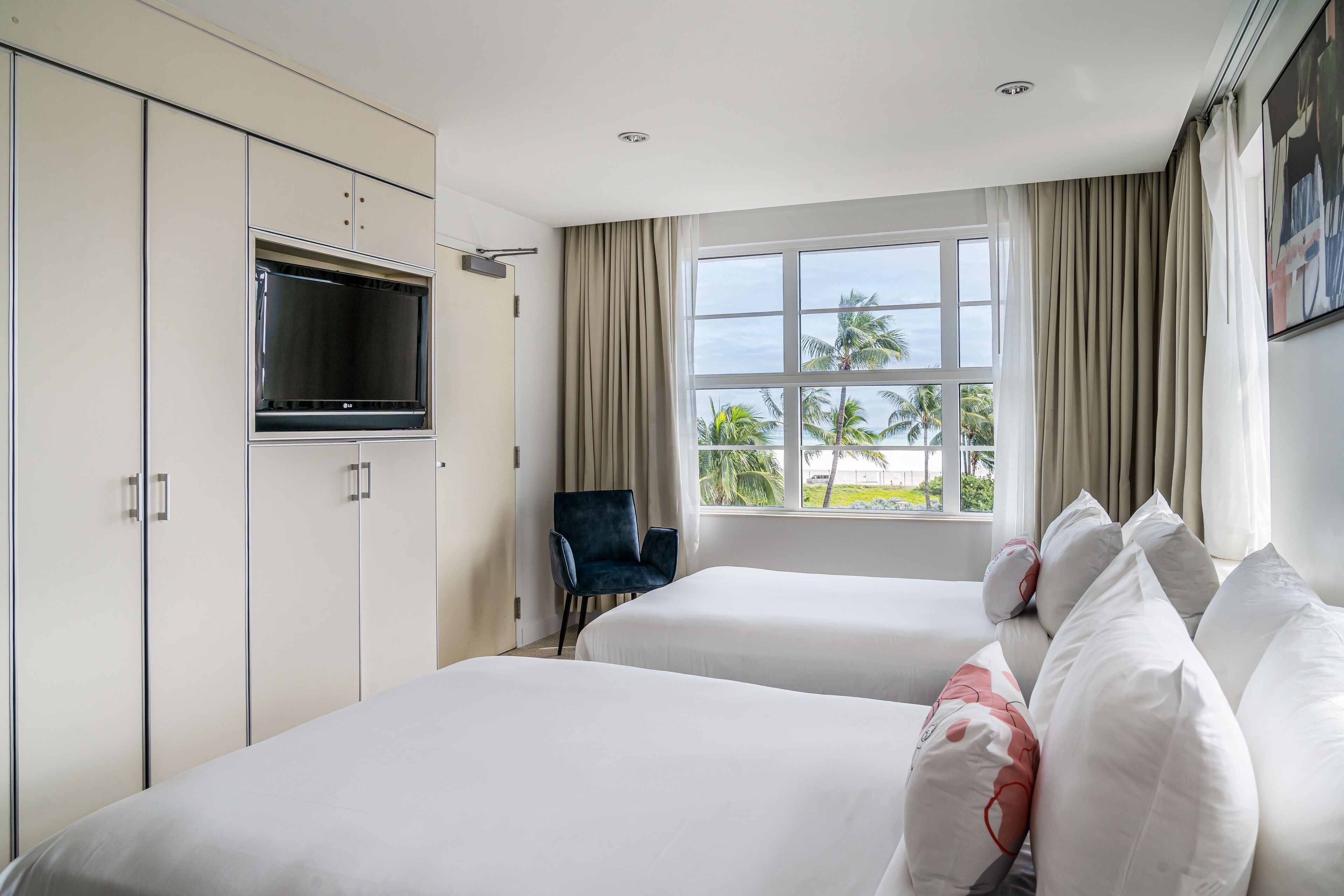 A hotel room with two beds, a TV, a chair, and a window with a view of palm trees.