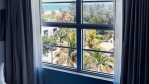 Ein Zimmer mit einem großen Fenster und Blick auf Palmen und einen Strand.