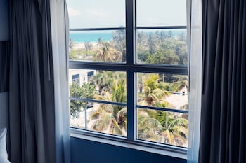 A modern living room with a grey sectional sofa, a small side table with a vase, and a view of palm trees through large windows. at Clevelander Hotel – Adults Only