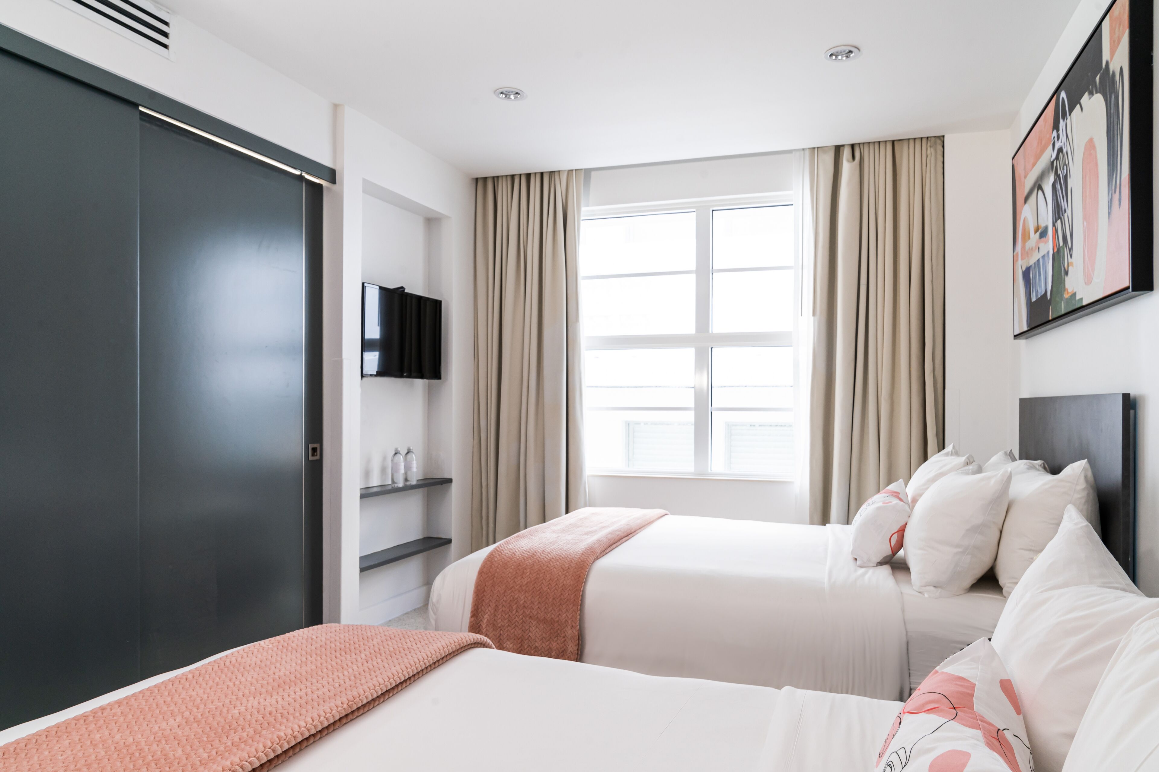 A hotel room with two beds, a TV, a wardrobe, and a window with curtains.