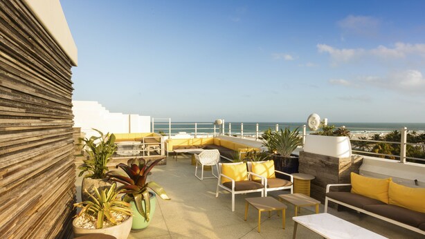Eine Dachterrasse mit Sitzgelegenheiten im Freien, Blumentöpfen und Blick aufs Meer.