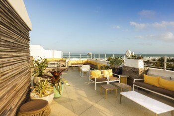A bed with a bottle of champagne and two glasses on a tray, a blue chair, and a view of palm trees through a window. at Clevelander Hotel – Adults Only