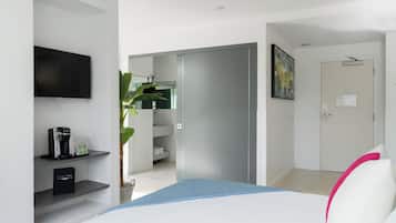 A modern hotel room with a flat-screen TV, a coffee machine, a plant, and a bed with a blue and white bedspread.