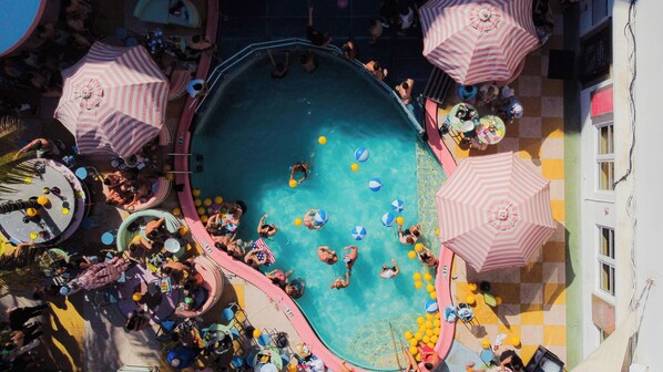 Un espace piscine doté de plusieurs parasols, de chaises longues et où l’on peut voir des gens pratiquer diverses activités.