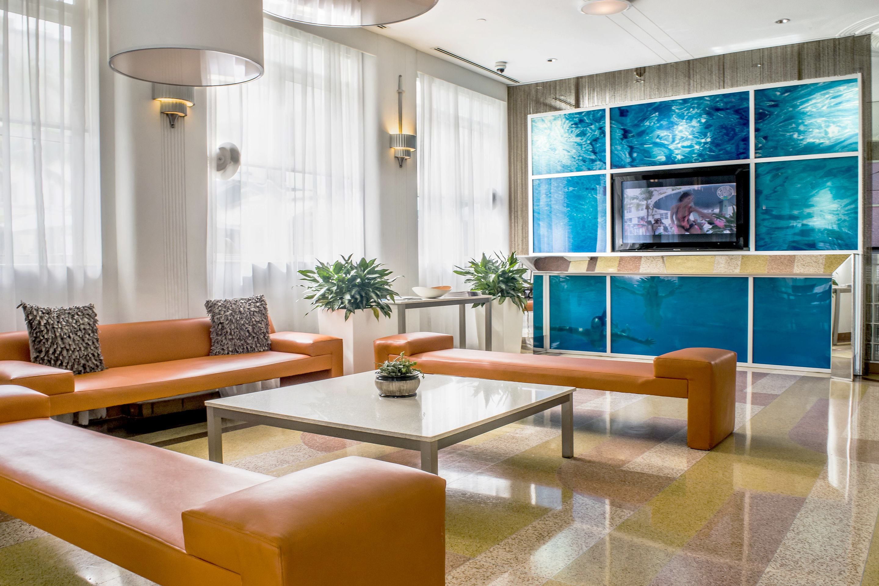 Una sala de estar moderna con sofás naranja, una mesa de centro y un televisor montado en una pared azulada.