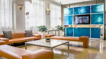 A modern living room with orange sofas, a coffee table, and a TV mounted on a blue-tinted wall.