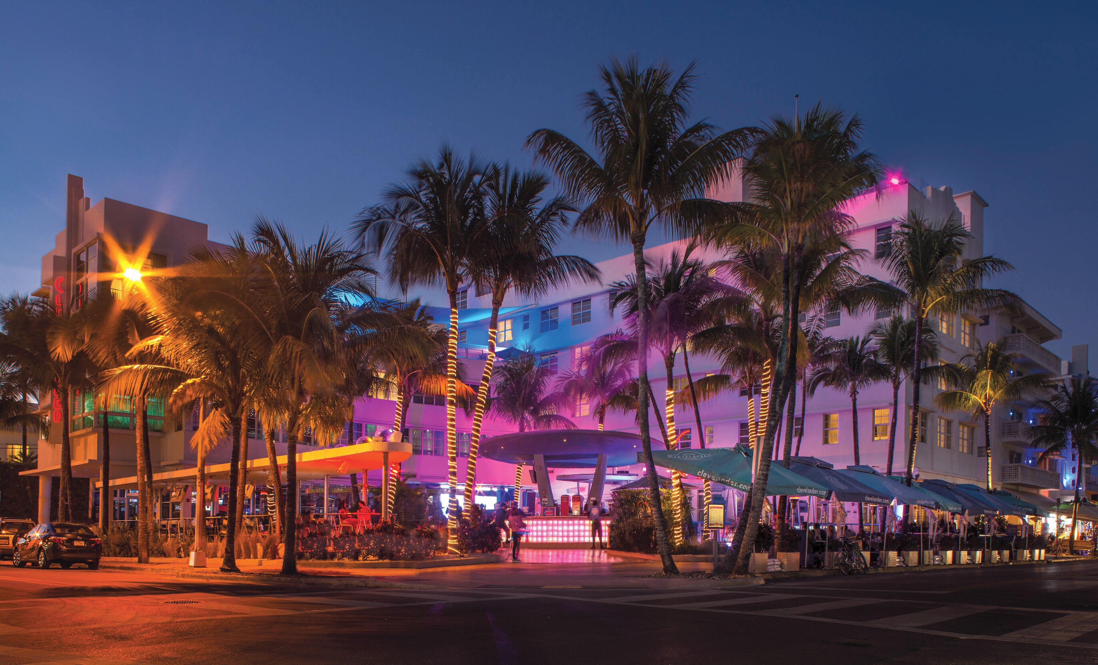 A hotel with multiple floors, outdoor seating areas, and palm trees.