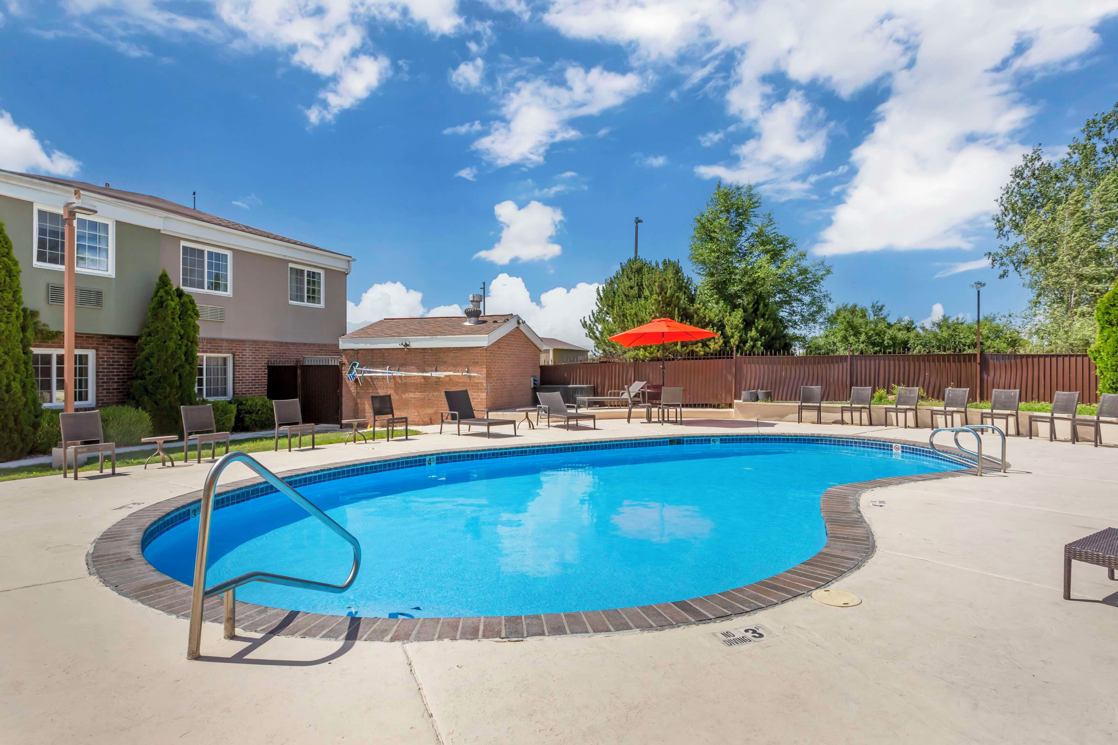 A swimming pool with a metal ladder, surrounded by lounge chairs and a red umbrella.