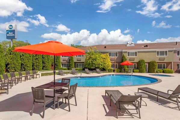A pool area with lounge chairs and umbrellas, a Best Western sign, and a building with multiple windows and a brick facade.