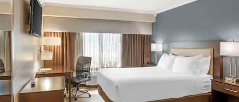 Una camera d'albergo con un letto grande, una scrivania, una sedia, un televisore e un comodino con una lampada.