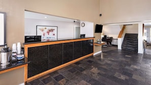 A hotel reception area with a black marble counter, a clock, and a flat-screen TV. - Best Western Mountain View Inn (Springville)