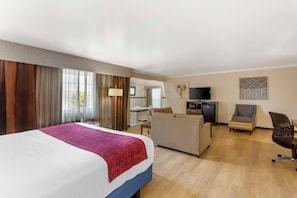 A hotel room with a bed, a desk, a sofa, a TV, and a bathroom visible through an open door.